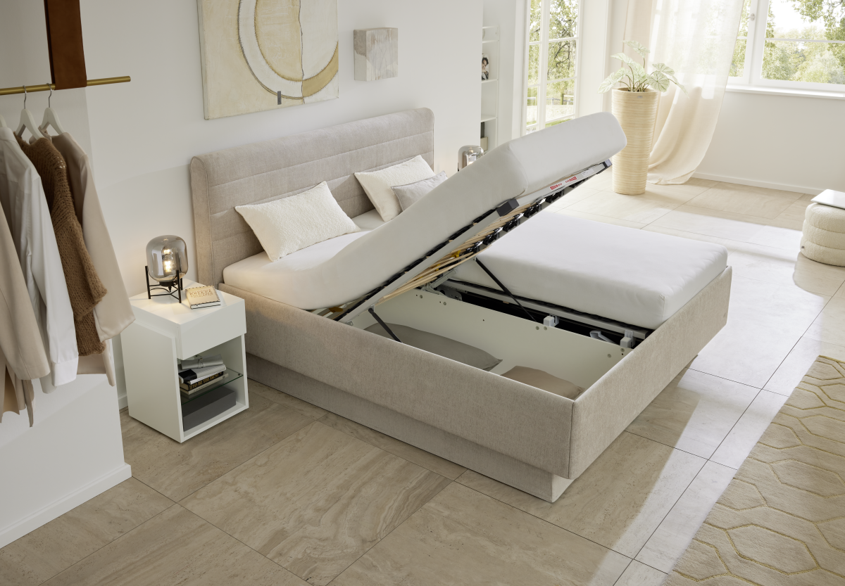 Boxspringbett mit geöffnetem Bettkasten in hellem Schlafzimmer, zeigt integrierten Stauraum.