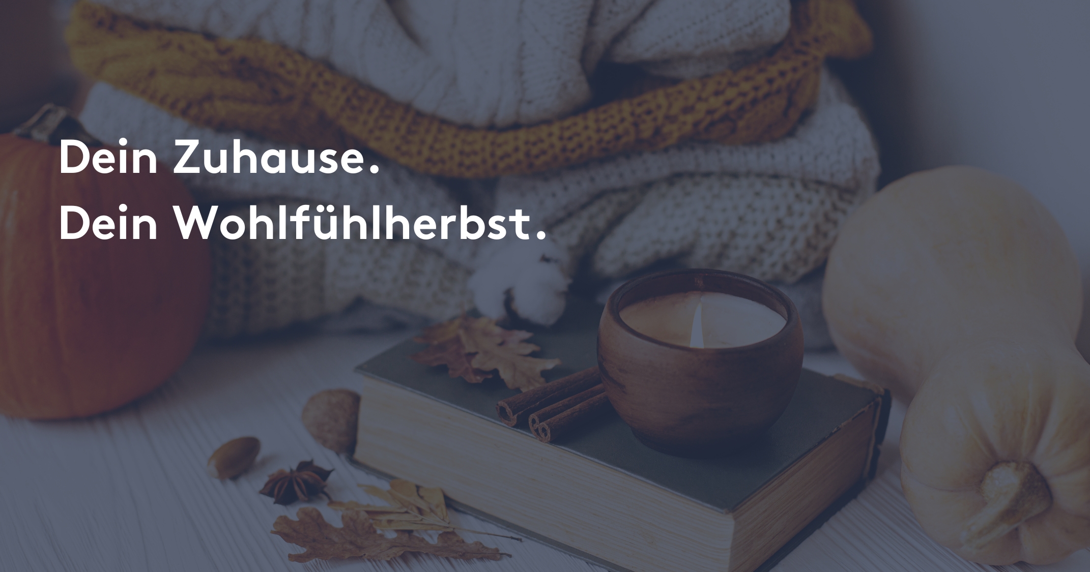 Herbstliche Wohlfühlatmosphäre mit Kürbissen, einem brennenden Duftkerzenglas auf einem Buch, Zimtstangen, getrockneten Blättern und einer grob gestrickten Decke im Hintergrund. Text: ‚Dein Zuhause. Dein Wohlfühlherbst