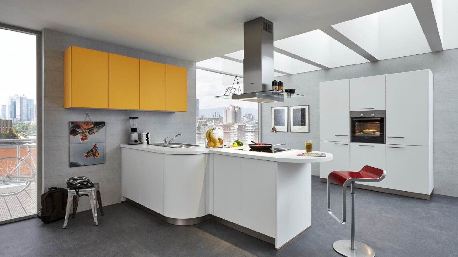 Moderne weiße Küche mit gelben Hängeschränken, Kochinsel und Barhockern unter einem großen Dachfenster.