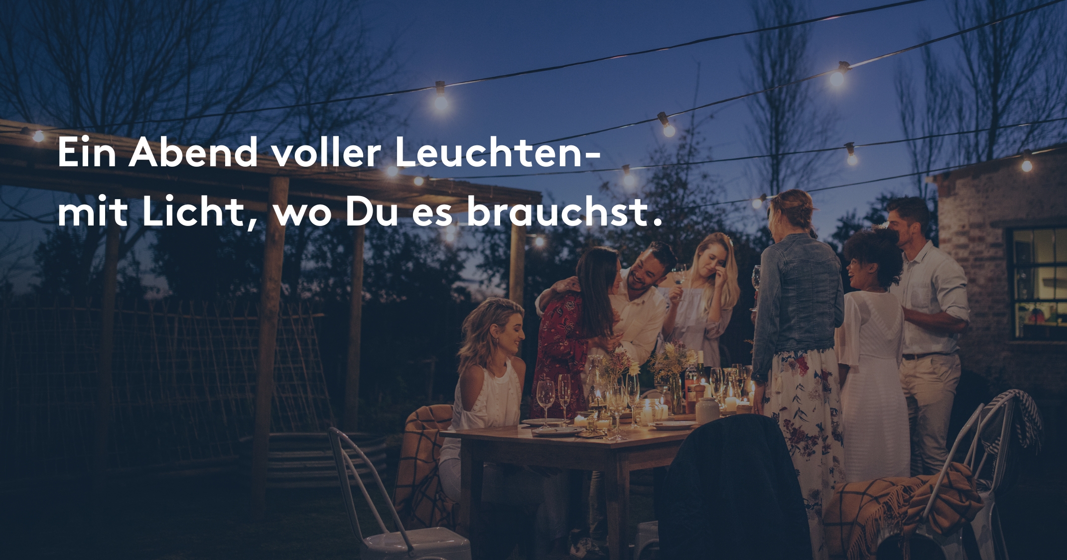 Gruppe von Freunden feiert abends im Garten unter Lichterketten, stimmungsvolle Outdoor-Beleuchtung.