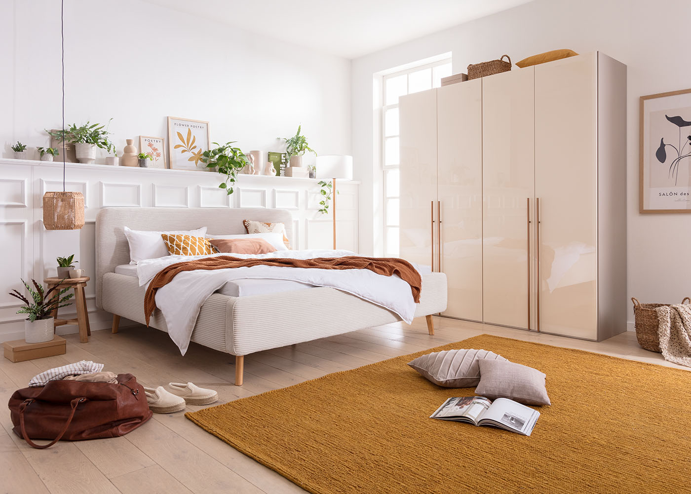 Ein Teppich in Ockergelb, ein braunes Plaid und eine Flechtlampe verleihen dem Schlafzimmer mit neutralfarbenen Bett eine Prise Mediterranen Stils.
