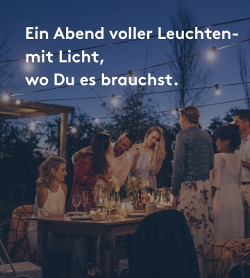 Gruppe von Freunden feiert abends im Garten unter Lichterketten, stimmungsvolle Outdoor-Beleuchtung.