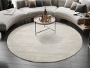 Runder, beiger Teppich im modernen Wohnzimmer mit grauem Holzboden, runder Couch und dekorativem Couchtisch.