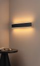 Moderne LED-Wandleuchte in Schwarz leuchtet an beiger Wand über rundem Tisch mit Brille und Zeitschrift.