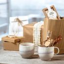 Zwei Keramiktassen, Geschenkboxen und Süßigkeiten auf Holztisch, stilvoll verpackt als Geschenkset.