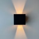 Moderne schwarze Wandleuchte strahlt warmes Licht nach oben und unten auf weiße Wand, minimalistisches Design.