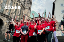 Motiviertes Team von Möbel RIEGER in roten Laufshirts jubelt nach erfolgreichem Zieleinlauf bei einem Stadtlauf – gemeinsam stark am Start