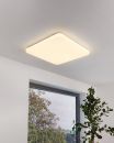 Moderne LED-Deckenleuchte in quadratischer Form an weißer Zimmerdecke, Fenster mit Ausblick und Pflanze.