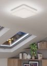 Moderne LED-Deckenleuchte leuchtet in hellem Raum mit Dachfenster, Regal, Büchern und Zimmerpflanze.
