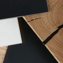 Nahaufnahme von Materialmustern in Schwarz und Weiss auf einer rustikalen Holzoberfläche mit deutlich sichtbarer Maserung und Riss – Darstellung von Farb- und Materialkontrasten im Möbelbereich.