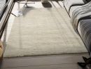 Beiger Hochflor-Teppich im modernen Wohnzimmer mit Sofa, Decke, Buch und viel Tageslicht am Fenster.