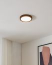 Runde LED-Deckenleuchte leuchtet in modernem Wohnzimmer mit weißer Decke, Vorhang und abstraktem Bild.