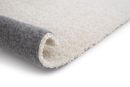 Beiger Hochflor-Teppich, teilweise aufgerollt, weiche Oberfläche, rutschfeste graue Unterseite.