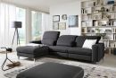 Modernes Wohnzimmer mit grauem Ecksofa, Bücherregal, Stehlampe, Teppich und großen Fenstern mit Tageslicht.