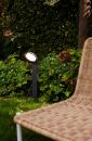 LED Wegeleuchte Polo 1-flg Moderne Gartenleuchte beleuchtet grüne Pflanzen neben einem Rattanstuhl im gepflegten Garten bei Tageslicht.