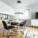 Moderne Küche mit Esstisch, schwarzen Stühlen, runder LED-Hängeleuchte und Tageslicht durch Fenster.