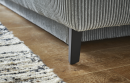 Nahaufnahme eines grauen Cordsofas mit schwarzen Metallfüßen auf Holzfußboden und gemustertem Teppich.