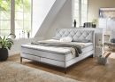 Modernes Boxspringbett mit grauem, gestepptem Kopfteil und weißer Matratze auf Metallfüßen, Schlafzimmermöbel.