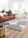 Frau entspannt auf rotem Sofa im modernen Wohnzimmer mit hellem Teppich, Holzboden und großen Fenstern.