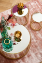 Drei runde Couchtische mit goldenen Gestellen, Spiegelplatten, Deko-Vasen und Snacks auf rosa Teppich.