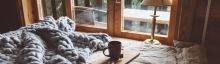 Einem Interieur im Chalet-Stil mit Blick aus dem Holzfenster verleihen Grobstrick-Plaid und Teetasse optische Wärme