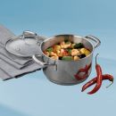 Edelstahltopf mit Garnelen, Gemüse und Kräutern, daneben zwei rote Chilischoten und ein graues Tuch.