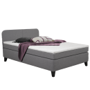 Graues Boxspringbett mit weißer Matratze, lila Decke und Kissen, modernes Schlafzimmermöbel, komfortabel.