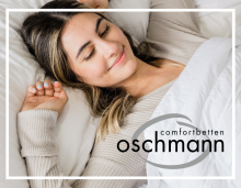 Junge Frau liegt entspannt und lächelnd in einem weißen Bett, eingekuschelt in eine weiche Decke. Sie trägt einen beigefarbenen Strickpullover. In der unteren rechten Ecke befindet sich das Logo „oschmann comfortbetten“