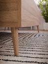 Nahaufnahme eines modernen Holzmöbels auf gestreiftem Teppich, mit grüner Zimmerpflanze im Hintergrund.