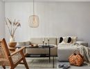 Modernes Wohnzimmer mit beigem Sofa, Holzmöbeln, Dekokissen, Teppich, Korbtasche und minimalistischer Beleuchtung.