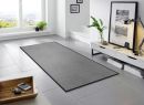 Moderner, grauer Teppichläufer im hellen Wohnzimmer mit großen Fenstern, Pflanzen und stilvoller Dekoration.