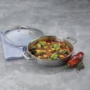 Gemüse-Ratatouille in Edelstahlpfanne mit Deckel, frischen Kräutern und roter Paprika auf grauem Untergrund.
