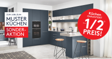 Moderne blaue Musterküche mit Kochinsel und Hockern; Jubiläumsaktion mit Hinweis auf Sonderpreise zum halben Preis in grossen Werbetafeln. Rabattdetails siehe Aktionsbedingungen.
