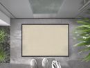 Beige Fußmatte vor Haustür auf grauem Boden, daneben weiße Sneaker und grüne Pflanzen, moderne Eingangsszene.