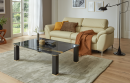 Modernes Wohnzimmer mit beiger Ledercouch, schwarzem Marmortisch, Teppich und großen Fenstern mit Gartenblick.