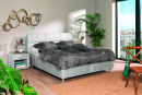 Modernes Boxspringbett mit grauem Polsterkopfteil, gemusterter Bettwäsche und mehreren Kissen im Schlafzimmer.