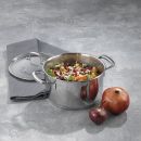 Edelstahltopf mit Gemüse und Reis auf grauer Arbeitsfläche, daneben Granatapfel und rote Zwiebel.