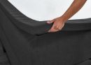 Hand zieht eine schwarze Matratzenauflage über ein Boxspringbett, Nahaufnahme, Schlafzimmer, Bettzubehör.