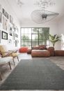 Modernes Wohnzimmer mit großen Fenstern, Ledermöbeln, grauem Teppich, Wandbildern und Zimmerpflanze.