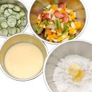 Küchenschüssel-Set Gourmet 4-teilig Vier Metallschüsseln mit Gurkenscheiben, Obstsalat, Eiermilch und Mehl mit Butter, Zutaten für Backrezepte.
