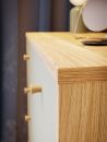 Nahaufnahme einer modernen Kommode aus hellem Holz mit runden Griffen, dekoriert mit Spiegel und Vase.