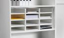 Weißes Regal mit mehreren Fächern, sortierten Dokumenten, Aktenordnern und Papierstapeln im Büro.