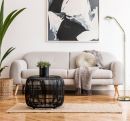 Modernes Wohnzimmer mit grauem Sofa, abstrakter Kunst, schwarzem Couchtisch und grüner Zimmerpflanze auf Holzfußboden.