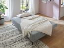 Modernes Schlafsofa mit heller Decke und Kissen im gemütlichen Wohnzimmer mit Holzboden und Tageslicht.