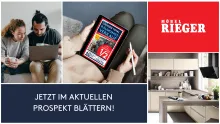 Junges Paar blättert online im Möbel Rieger Prospekt mit Angeboten, moderne Küche im Hintergrund.