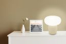 Weiße Kommode mit Lampe, Vase mit Rose und gerahmtem Foto eines Stegs bei Sonnenuntergang, minimalistisches Design.