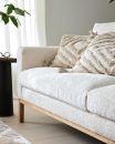 Helles Sofa mit Holzfüßen, dekoriert mit strukturierten Kissen im modernen Wohnzimmer, Tageslicht, Pflanzen.