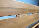 Holzbank aus hellem Holz mit klarer Maserung, moderne Sitzfläche, Detailaufnahme vor blauem Hintergrund.