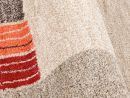 Nahaufnahme eines modernen Teppichs mit beigen, roten und orangen Streifen, weiche Hochflor-Struktur.