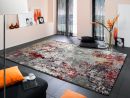 Moderner Wohnzimmerteppich in Grau-Rot auf dunklem Boden, mit orangen Kissen und stilvoller Dekoration.